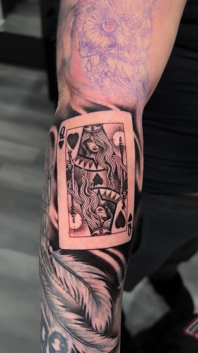 Queen of Hearts playing card tattoo on a forearm with owl sketch above