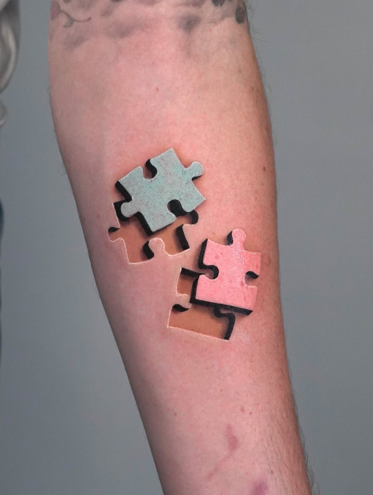 Two 3D puzzle pieces in teal and pink tattooed on a forearm.