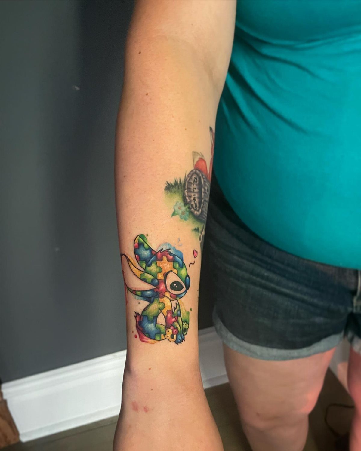 Stitch character tattoo on a forearm filled with colorful puzzle piece patterns.