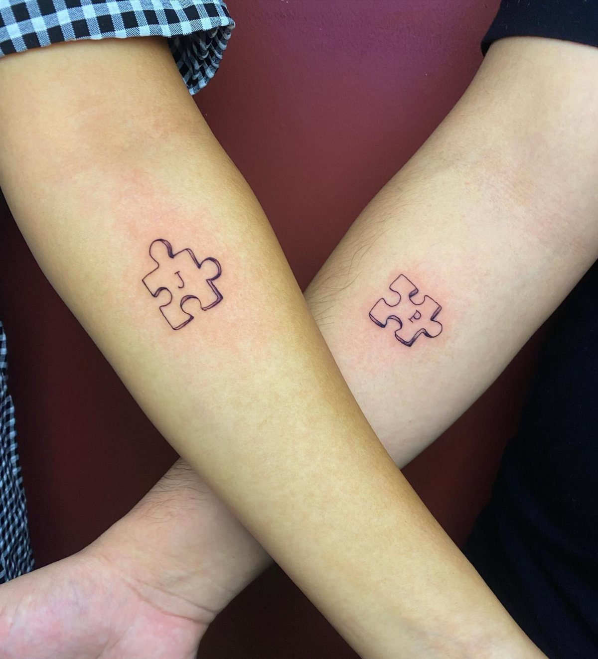 Two crossed forearms each with a small black outline puzzle piece tattoo.