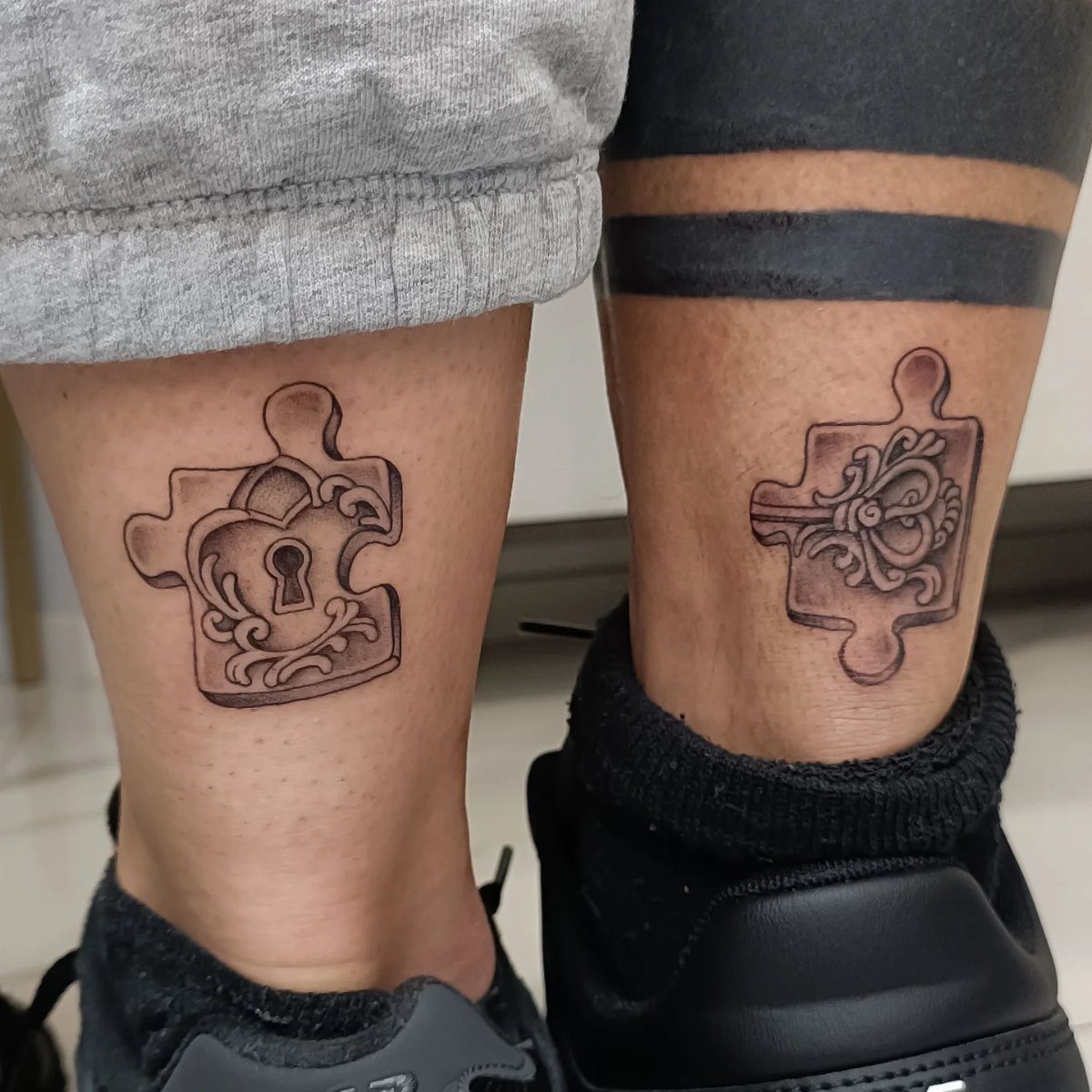 Matching puzzle piece tattoos on two ankles, one with a keyhole and one floral.