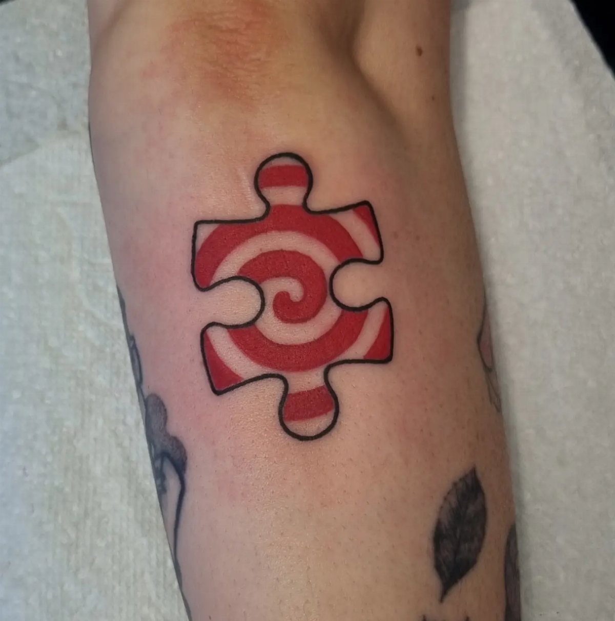 Puzzle piece tattoo with a red and white spiral on a person's arm.