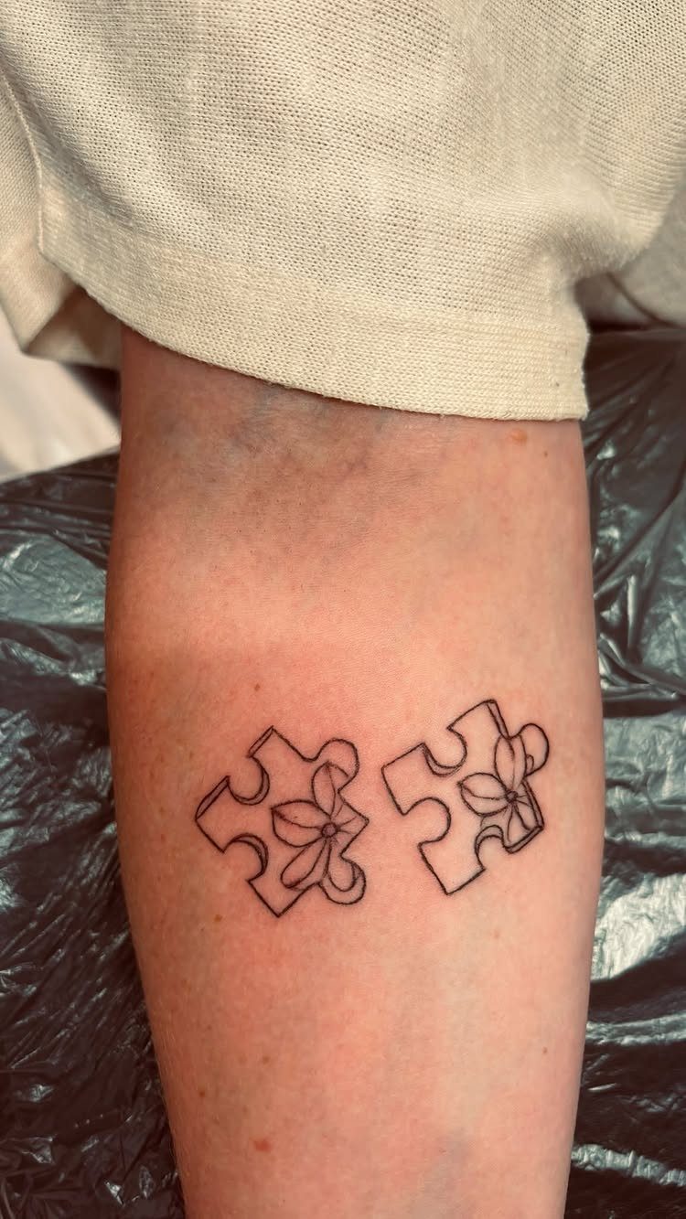 Two puzzle piece tattoos with small flowers inside on a person's forearm
