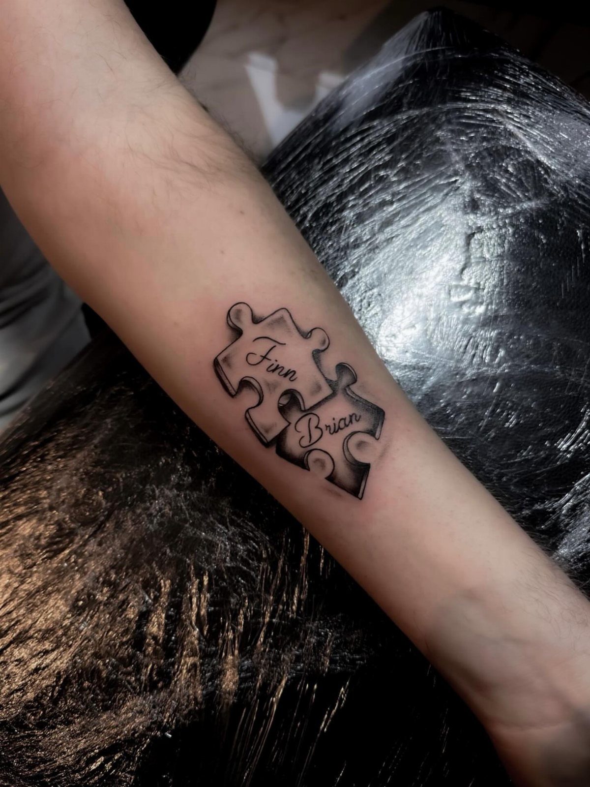 Two interlocking puzzle piece tattoos on a forearm with the names Finn and Brian.