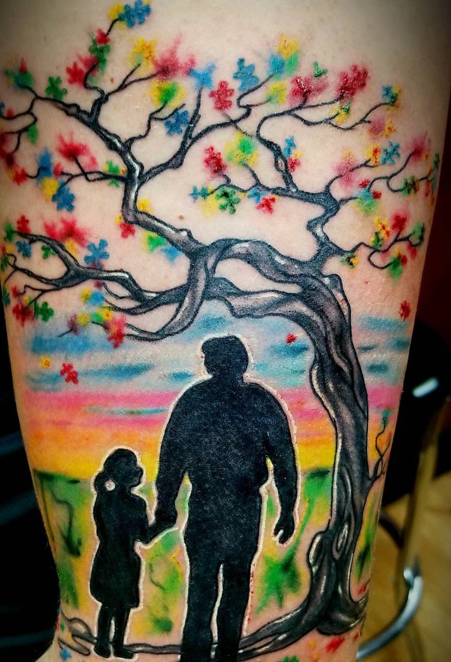 Tattoo of a man and child silhouette under a tree with puzzle piece leaves.
