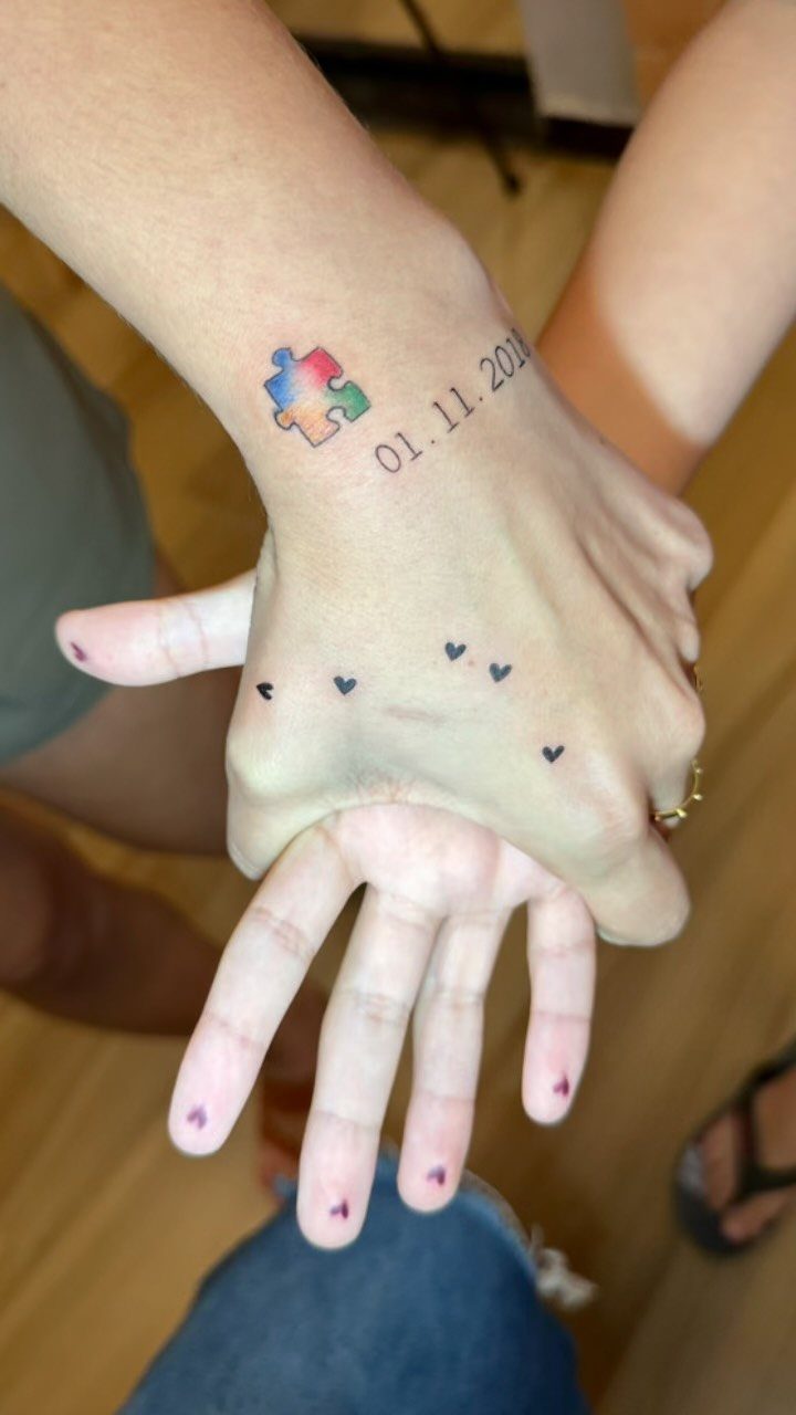 Rainbow puzzle piece tattoo on a wrist next to a date and hearts.