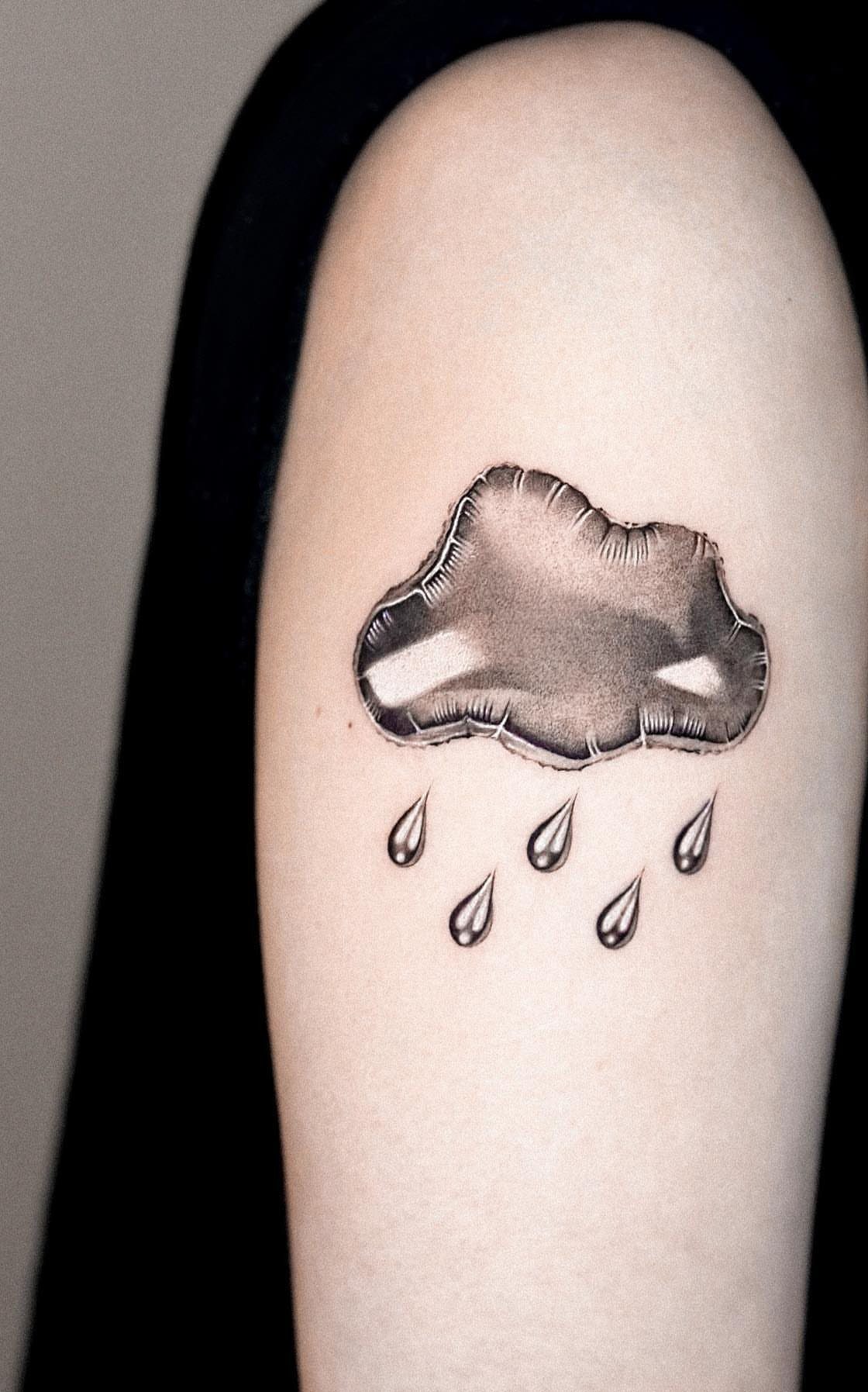 Fluffy cloud tattoo with teardrop raindrops on a person's upper arm.