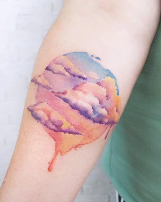Watercolor cloud tattoo with purple and orange hues and a single drip.