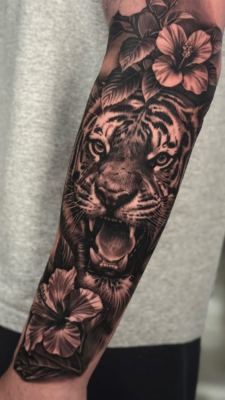 Roaring tiger head tattoo with hibiscus flowers on a person's forearm.
