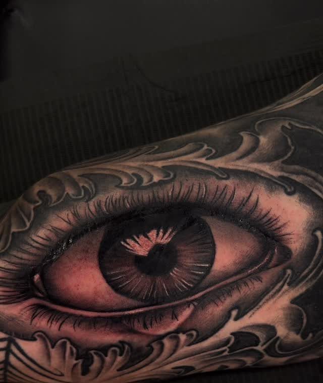 Detailed eye tattoo with a reflection in the pupil and ornate swirling patterns.