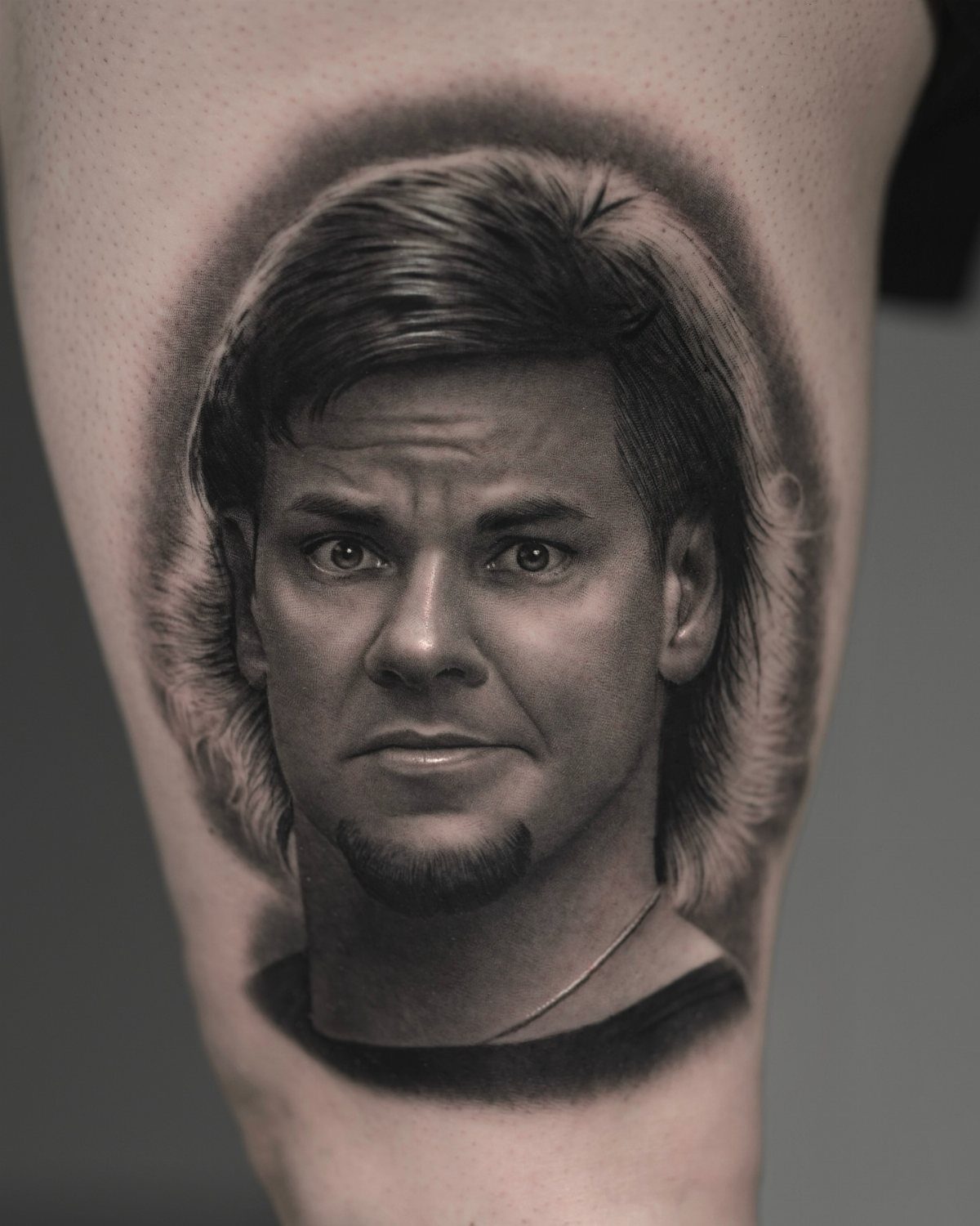 Realistic black and grey portrait tattoo of a man's face on skin.