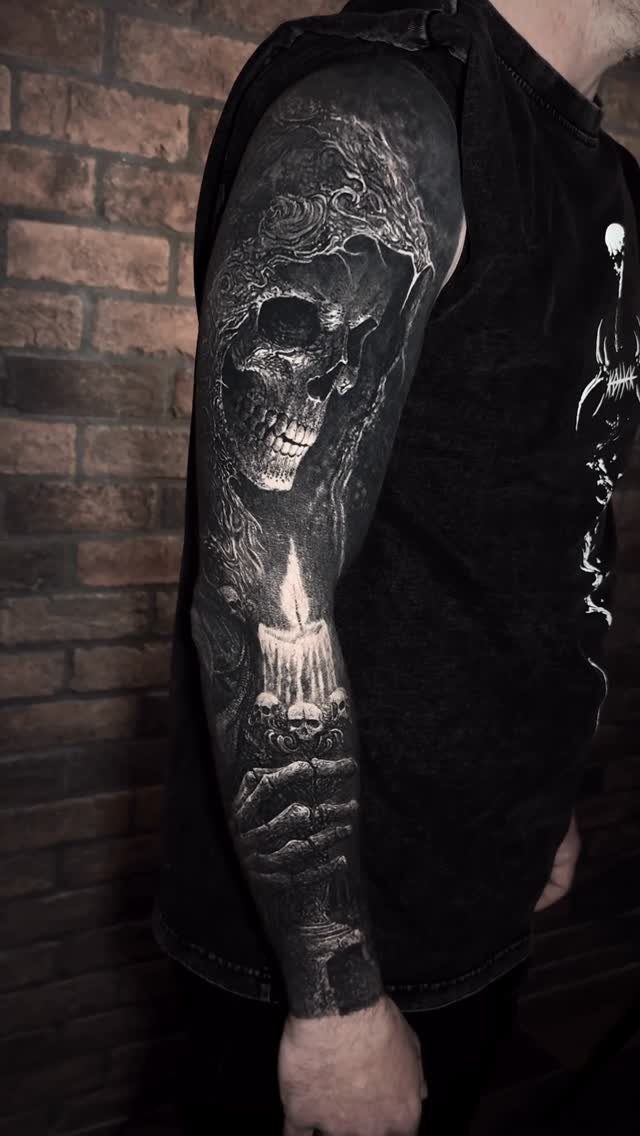 Realistic black and grey tattoo of a skull and candle on a man's arm.