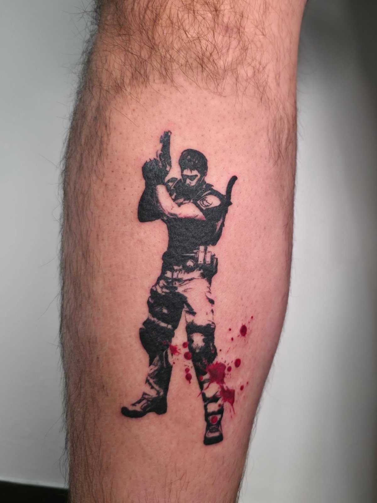 Chris Redfield tattoo on a leg featuring a soldier with a handgun and blood.