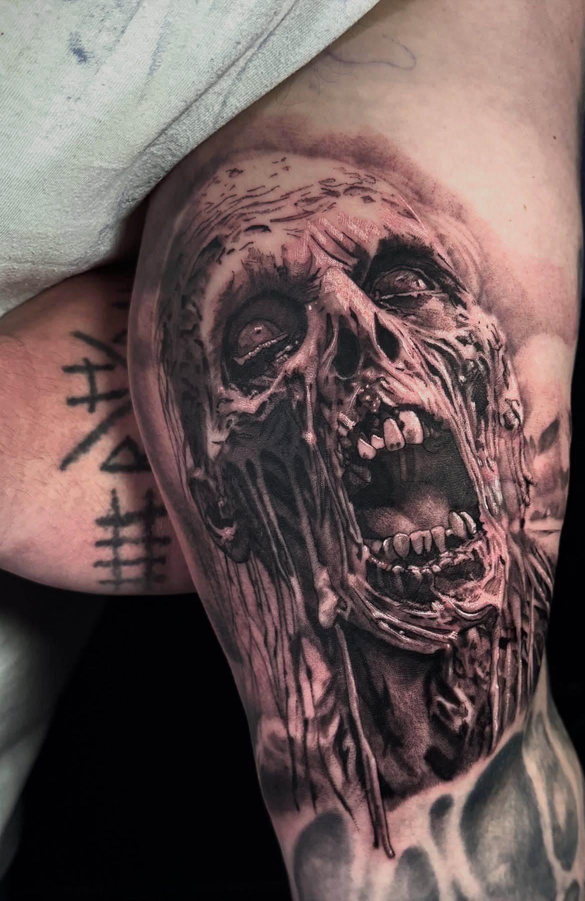 Zombie head tattoo with decaying skin and open mouth on a person's arm.
