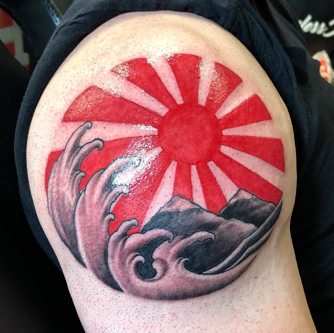 Rising sun tattoo with red rays, grey waves and mountains on a shoulder