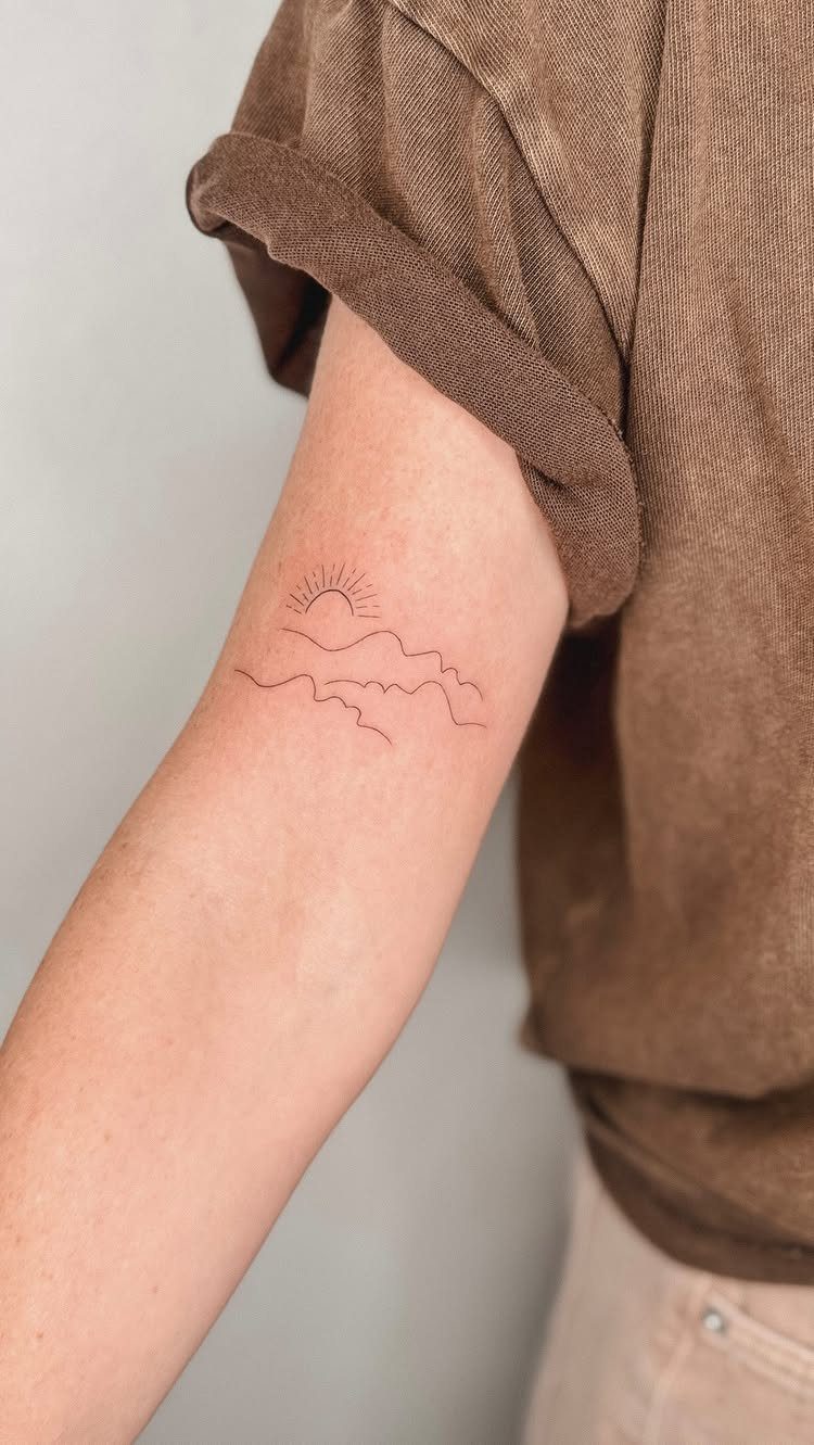 Fine line tattoo of a rising sun and mountains on a person's arm