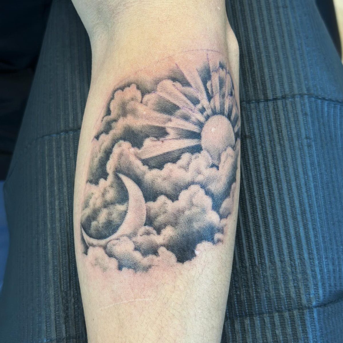 Sun and crescent moon tattoo with clouds on a person's forearm