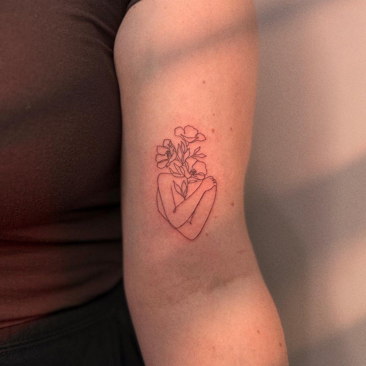 Fine-line tattoo of a person hugging themselves with flowers blooming from their head.