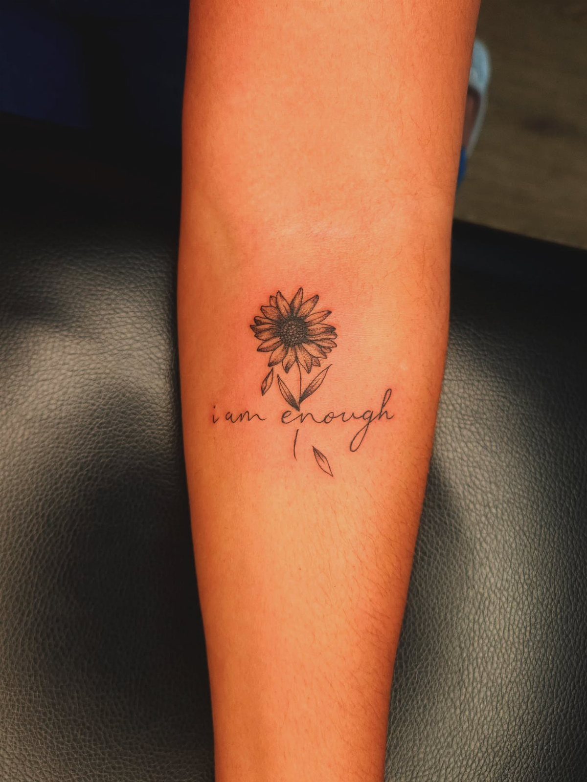 Sunflower tattoo on a forearm with the cursive text i am enough