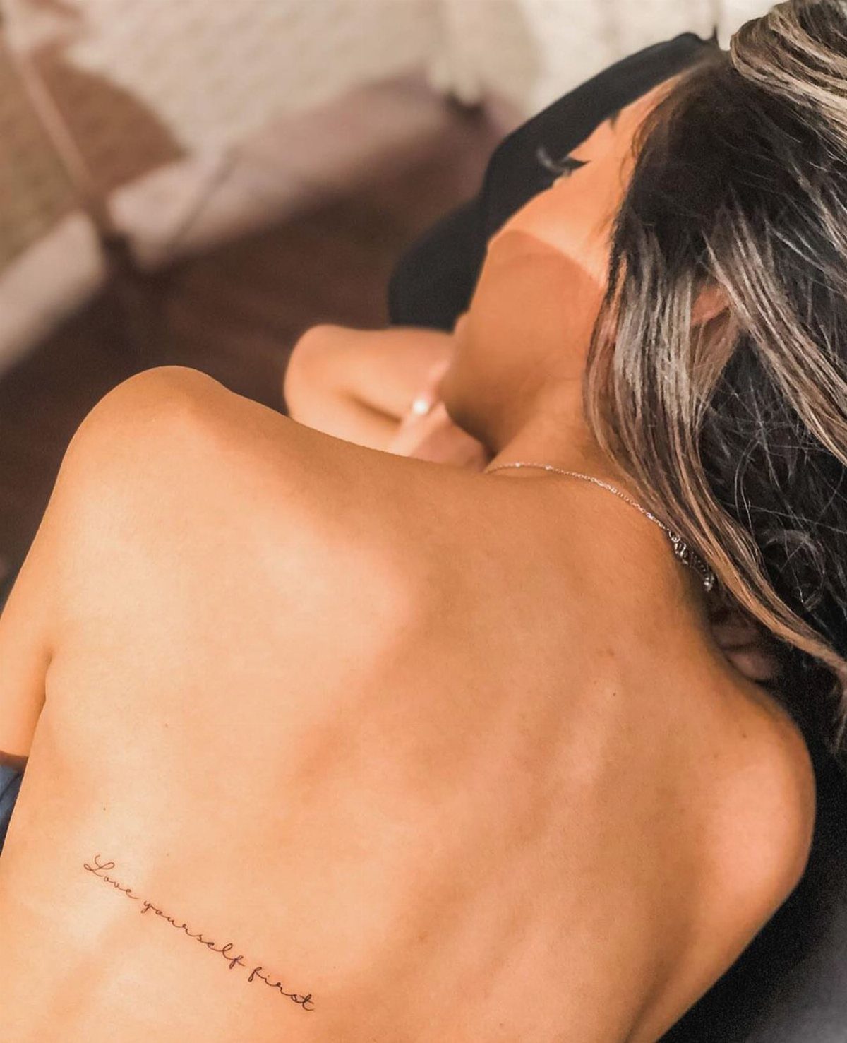 Cursive tattoo reading love yourself first on a person's lower back