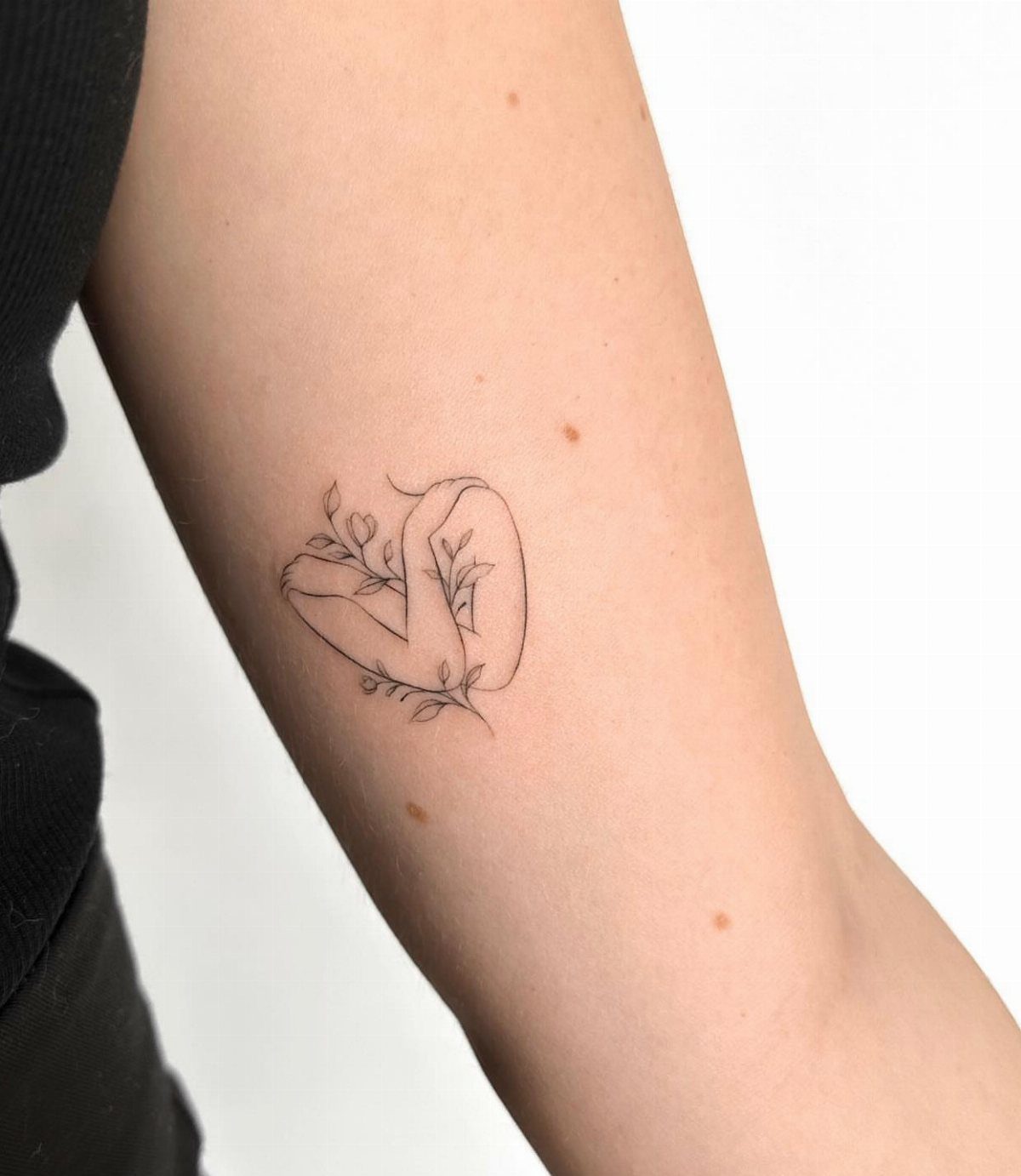 Fine-line tattoo of a woman hugging herself with floral accents on an arm
