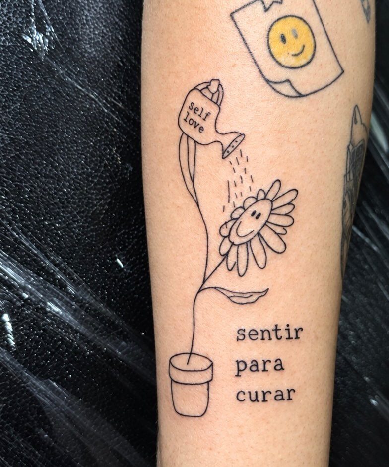 Self love tattoo of a smiling flower being watered with Portuguese text on skin
