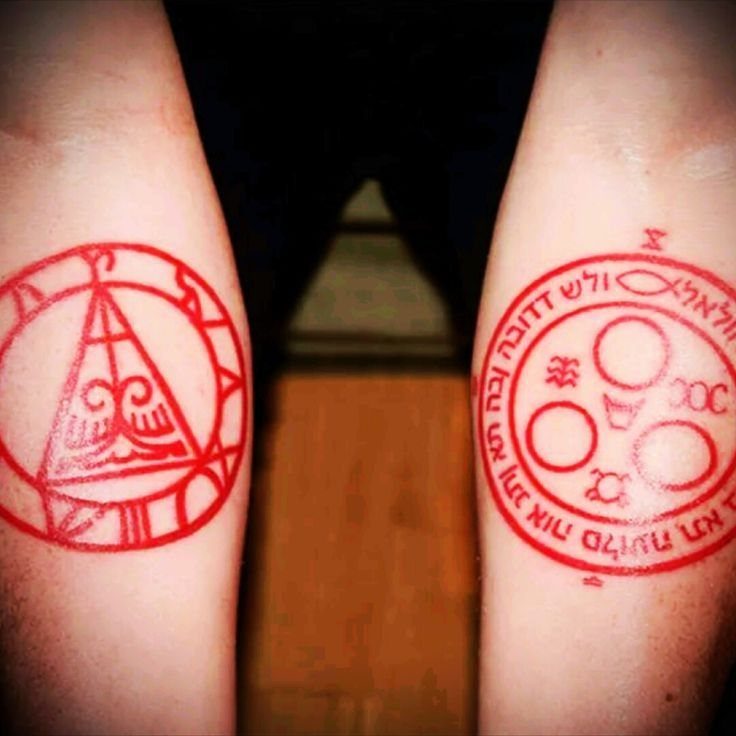 Red occult symbol tattoos on two inner forearms with geometric designs and script.