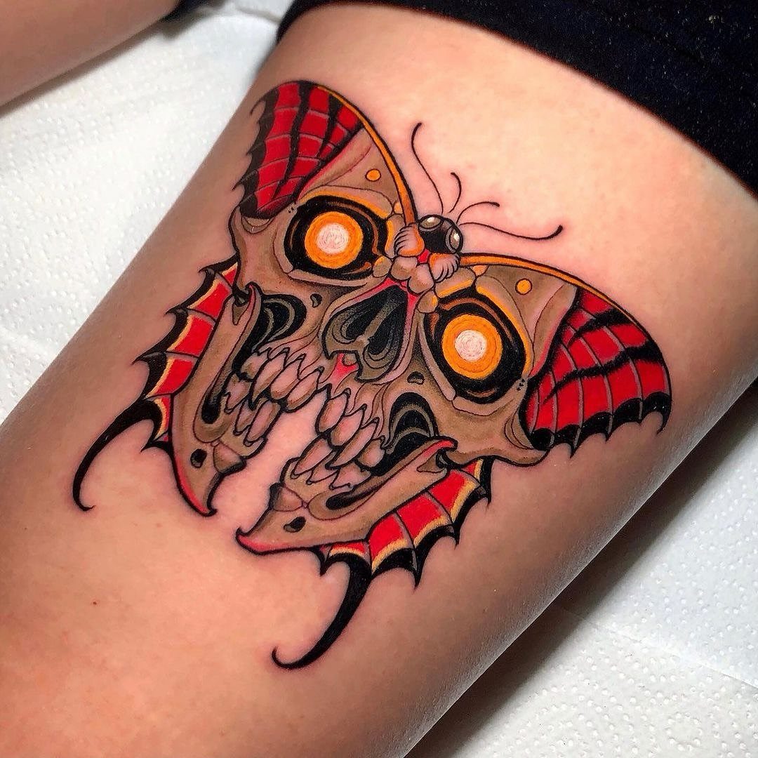 Butterfly skull tattoo with red wings and glowing yellow eyes on skin.