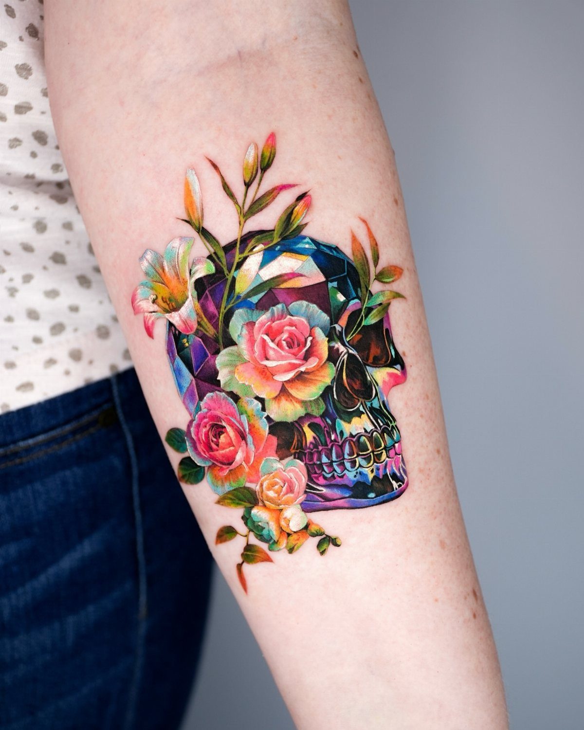 Crystal skull tattoo with colorful roses and floral accents on a person's arm.