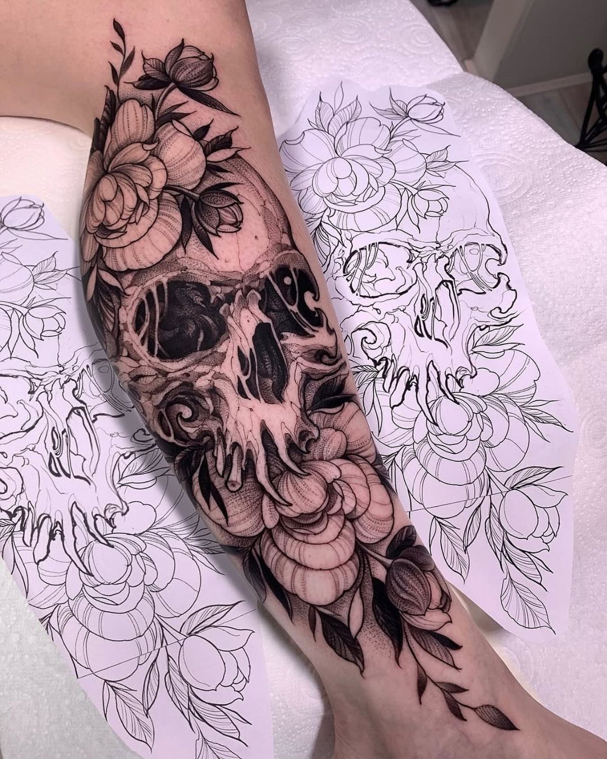 Skull tattoo with roses and leaves on a lower leg next to stencils.