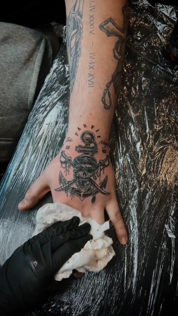 Pirate skull and anchor tattoo on a hand being wiped by a tattoo artist.