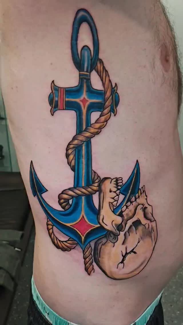 Blue anchor tattoo wrapped in rope with a human skull on a torso