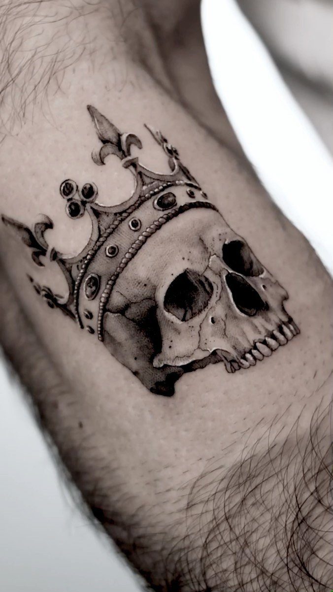 Realistic black and grey tattoo of a human skull wearing an ornate jeweled crown.