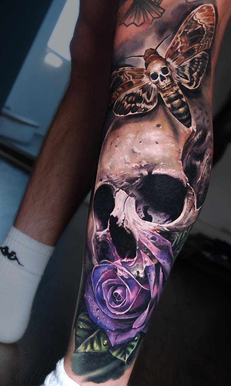 Realistic skull tattoo with a purple rose and a death's-head hawkmoth on forearm.