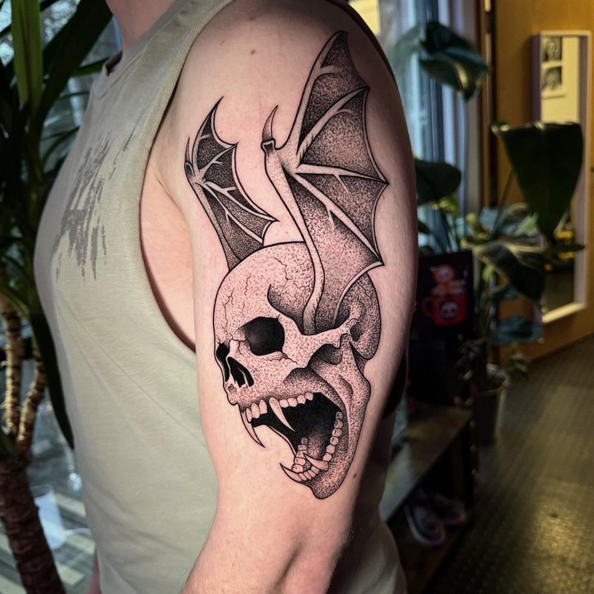 Screaming skull tattoo with bat wings on a person's upper arm