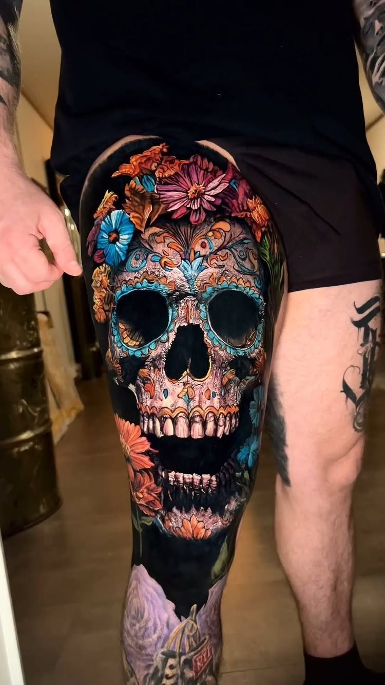 Sugar skull tattoo on a thigh with colorful flowers and intricate patterns.