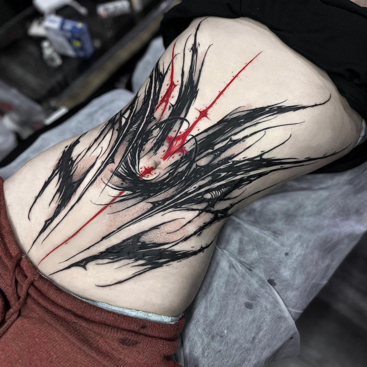 Abstract black and red tattoo with sharp lines on a person's lower back.