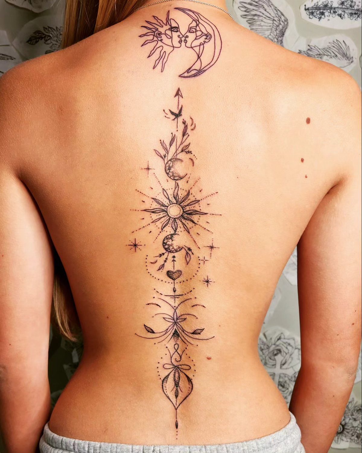 Celestial spinal tattoo featuring suns, moons, and stars on a person's back.