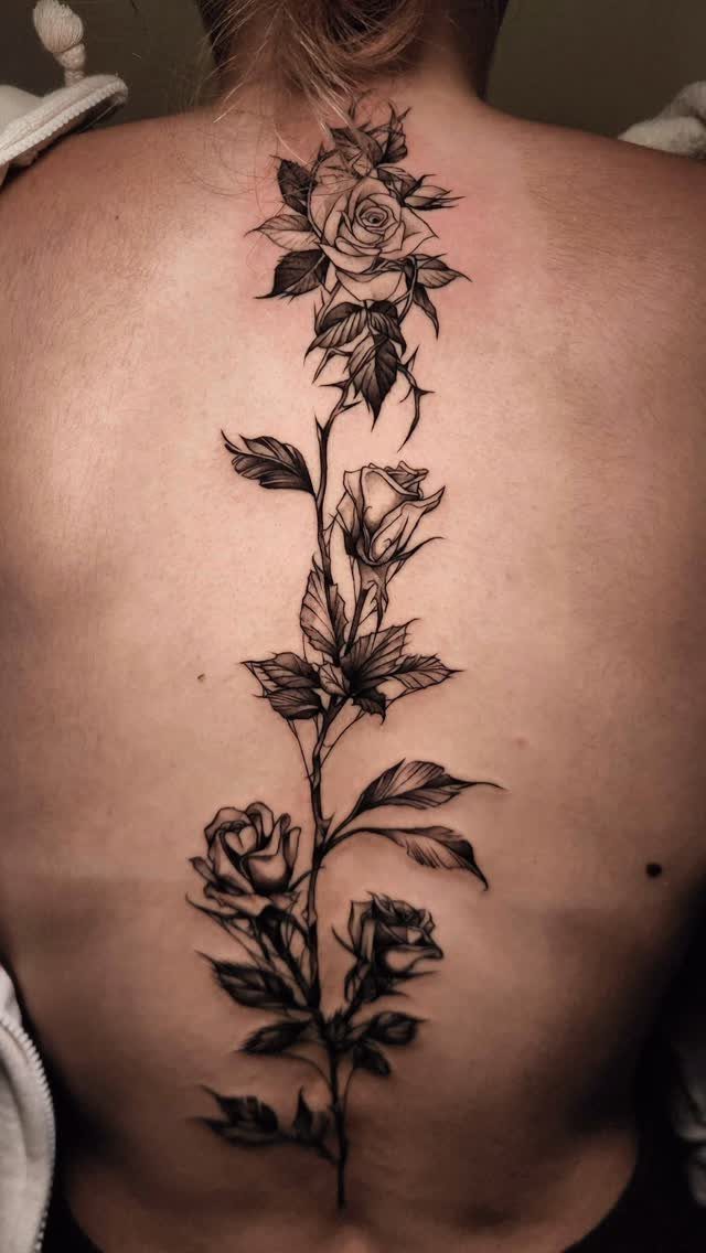 Rose stem tattoo with blooming flowers running down the center of a back.