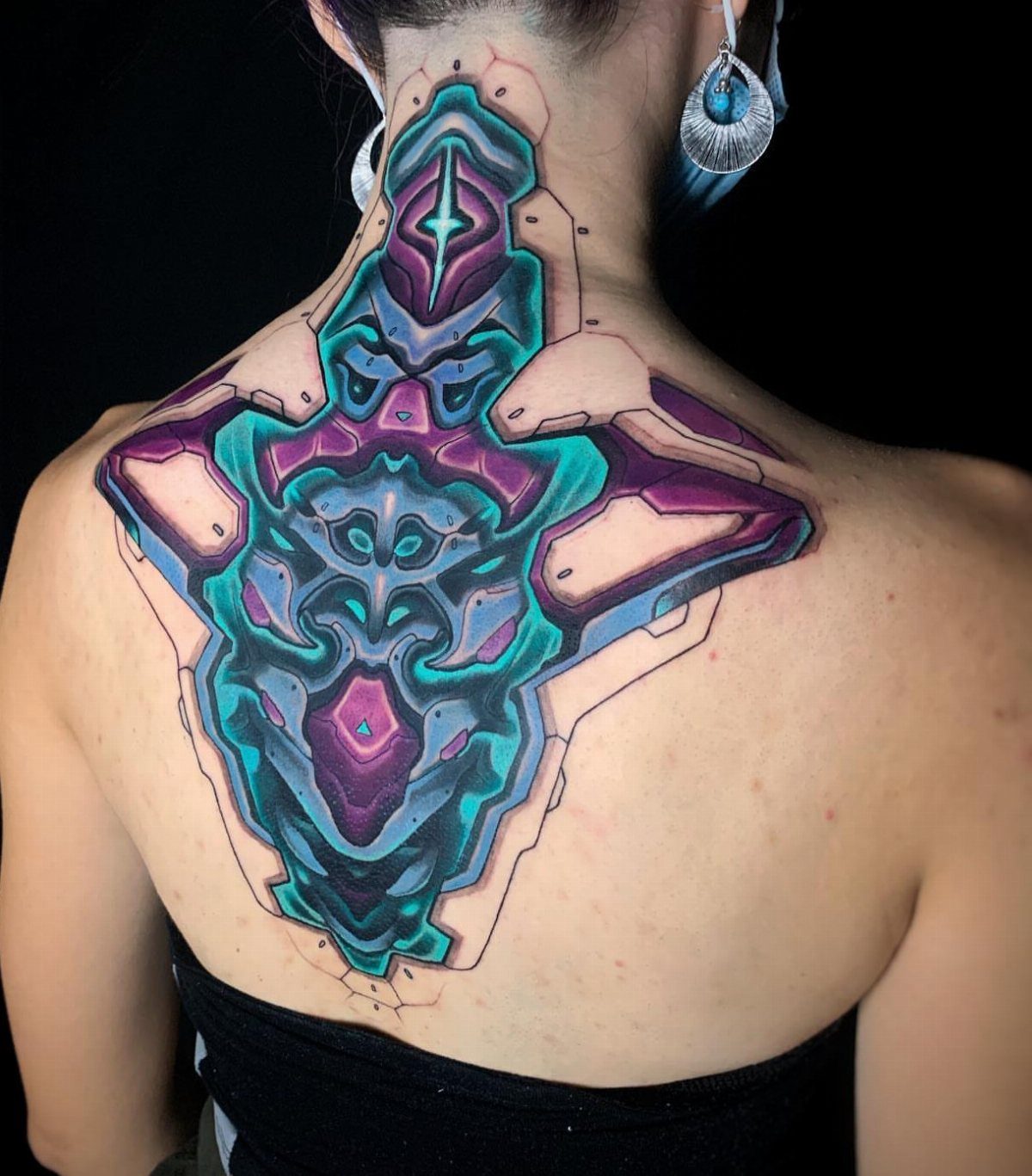 Biomechanical tattoo in teal and purple on a person's upper back and neck.