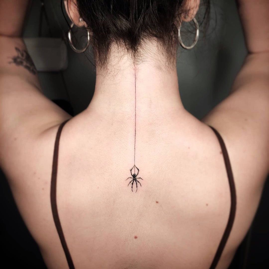 Spider tattoo hanging from a thin line on a person's upper spine