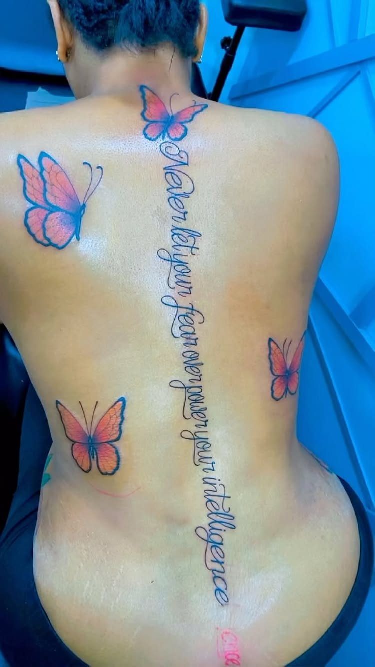 Person's back with a spinal quote tattoo and orange butterfly tattoos.