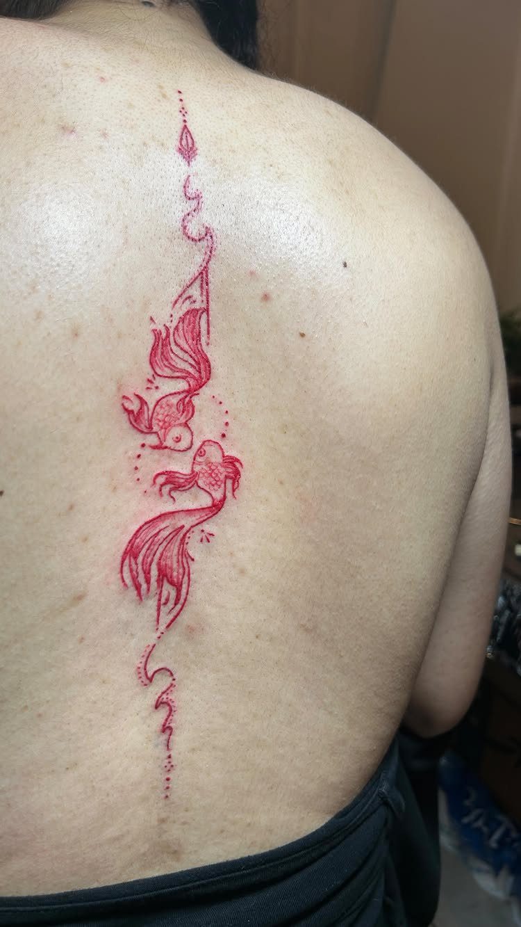 Red ink tattoo of two koi fish with flowing fins along a spine