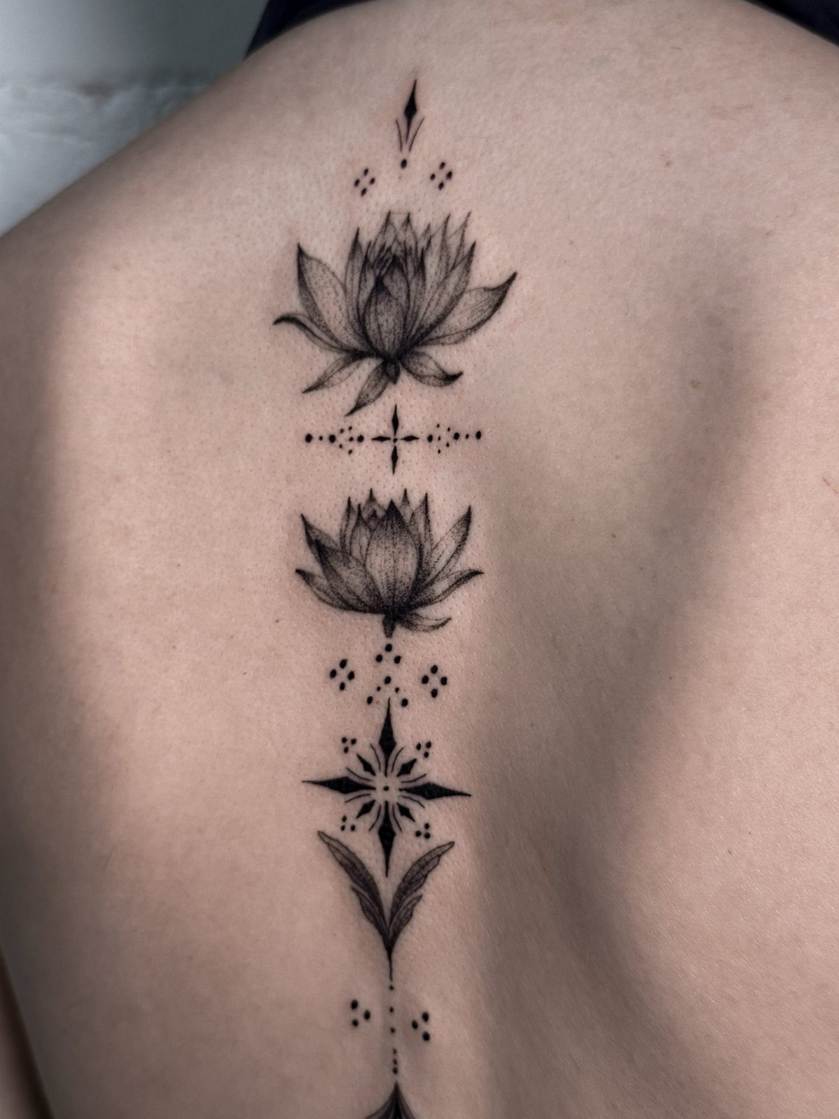 Lotus flower tattoo with geometric patterns running vertically down a person's spine.
