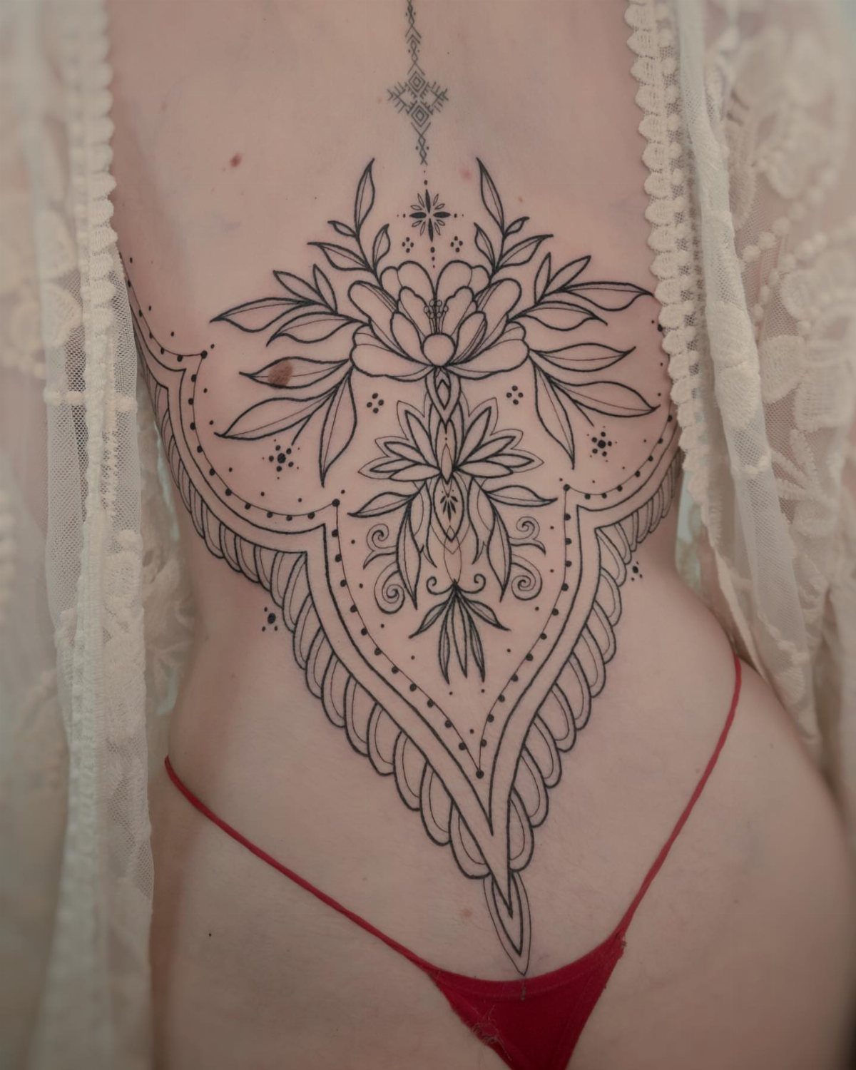 Intricate black ink ornamental tattoo with floral and geometric patterns on a lower back.