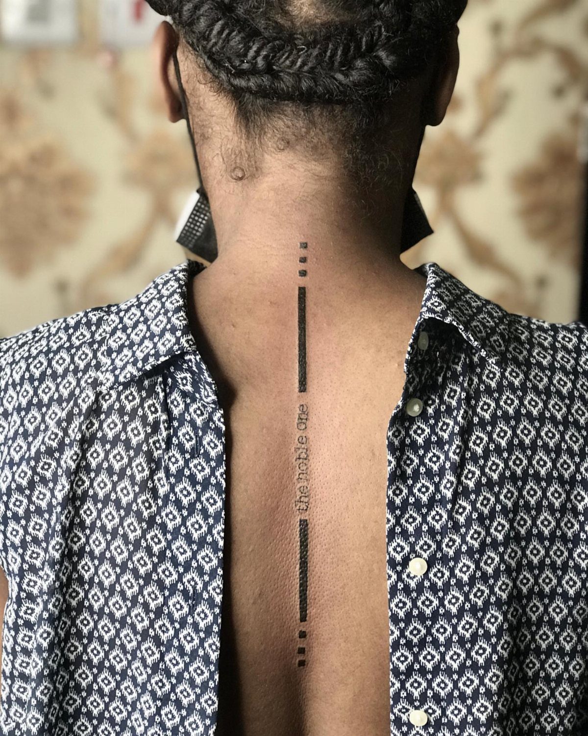 Vertical black line tattoo with text running down a person's spine