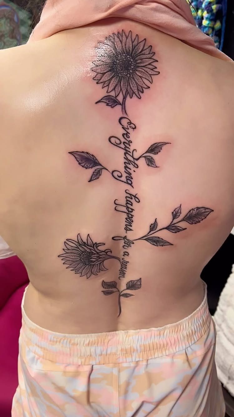 Sunflower spine tattoo with cursive text and leaves on a person's back