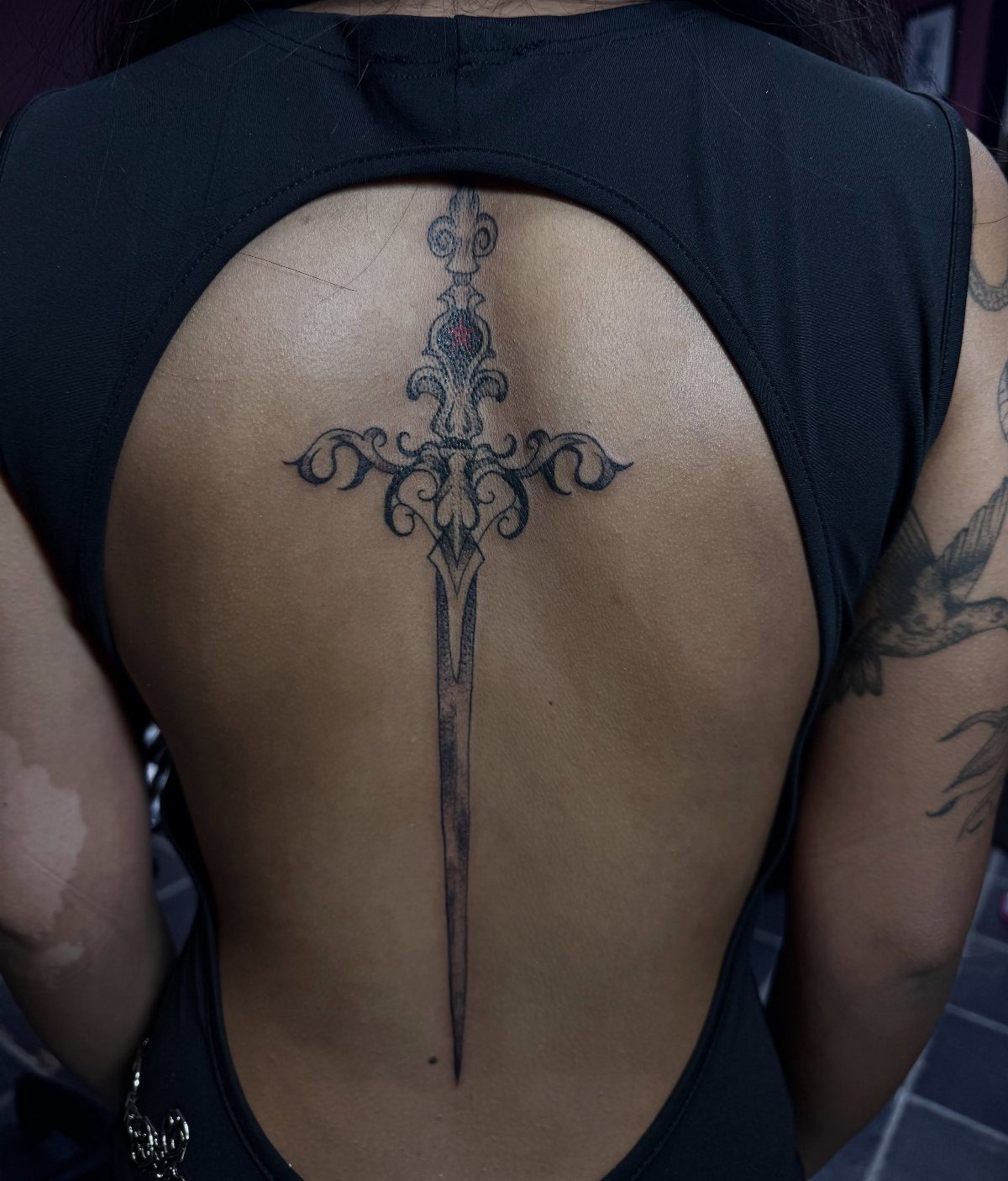 Ornate sword tattoo centered vertically along the spine of a person's back.