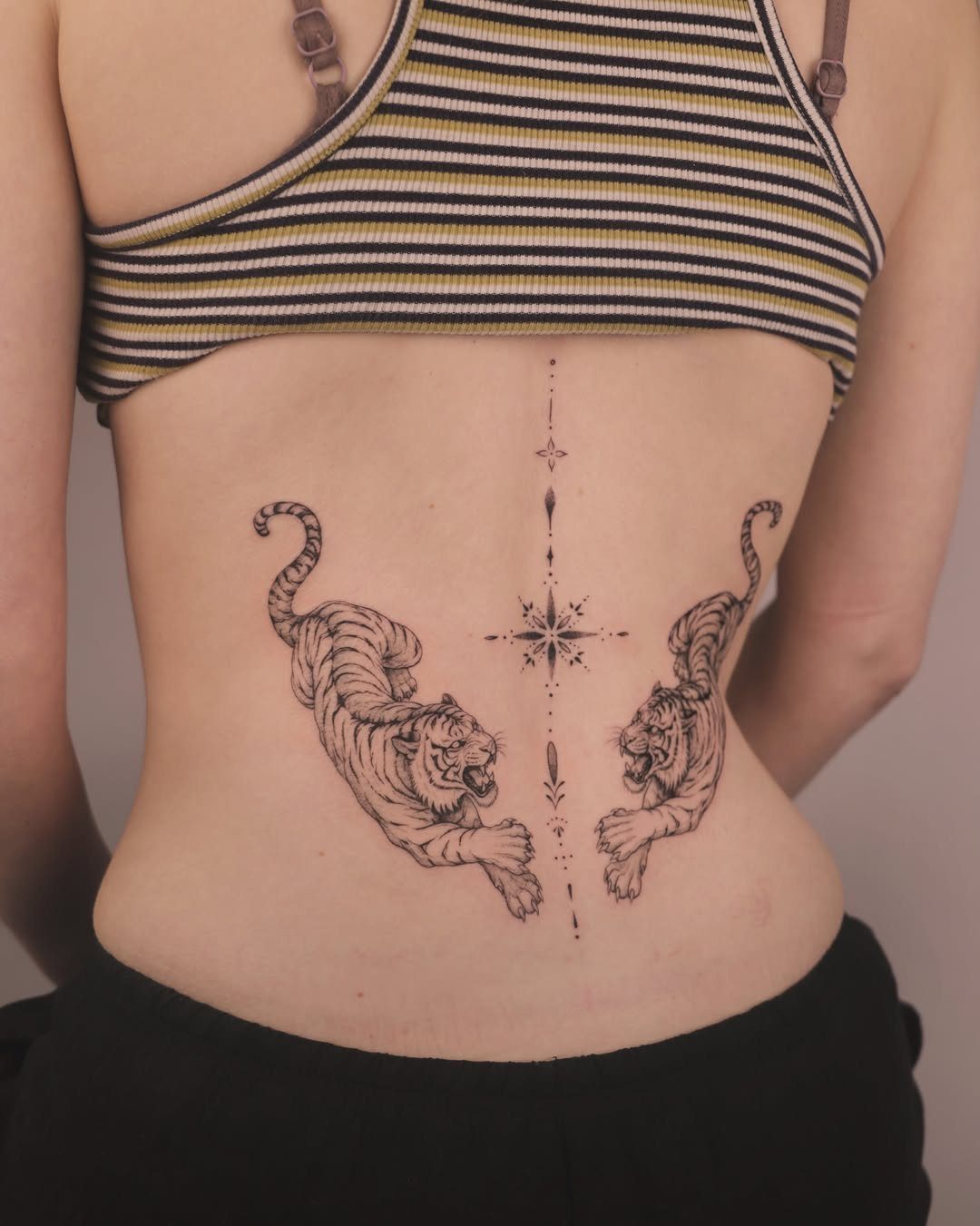 Two tiger tattoos flanking a thin vertical line on a person's lower back.
