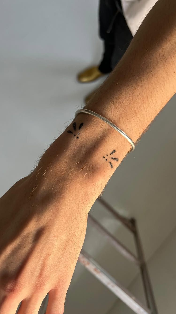 Wrist with two small black dot tattoos and a thin silver bracelet.